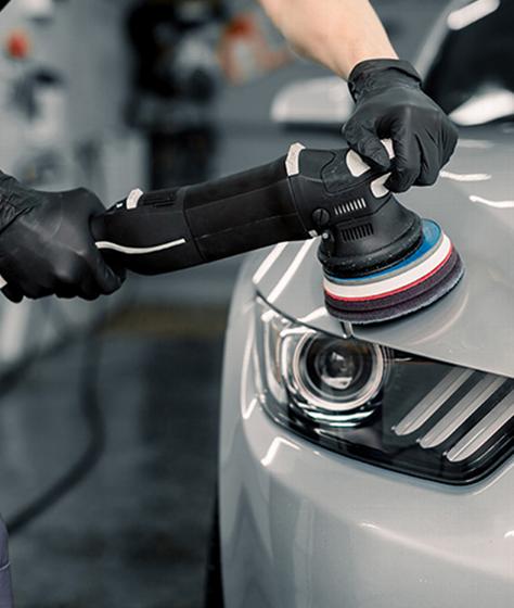 person using a dual action polisher on a gray car headlight for surface enhancement and paint correction