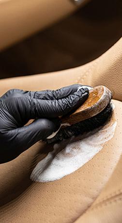 person cleaning leather seat with brush and foam during car detailing process