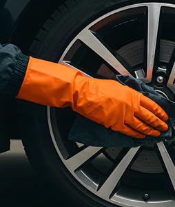 person cleaning a car wheel with a microfiber cloth wearing orange rubber gloves showing car maintenance techniques for three clean wheels